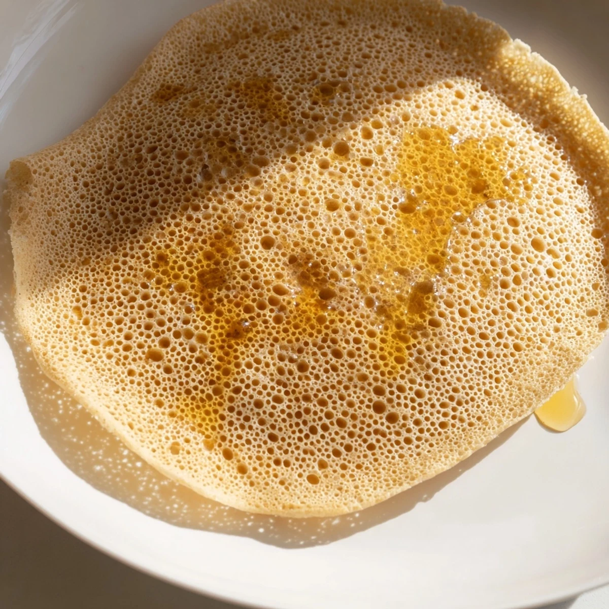 Golden, bubbly Moroccan Baghrir crepes are ready, drizzled with melted butter and sweet honey.