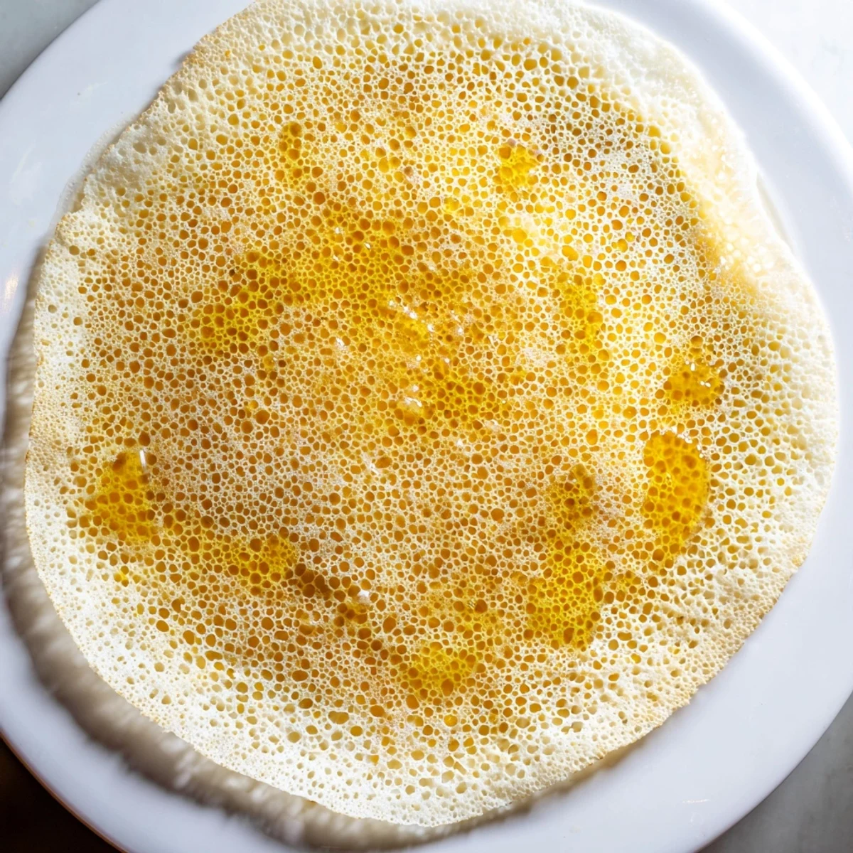 Homemade Moroccan Baghrir, a spongy pancake, topped with glistening honey butter for a delightful breakfast.