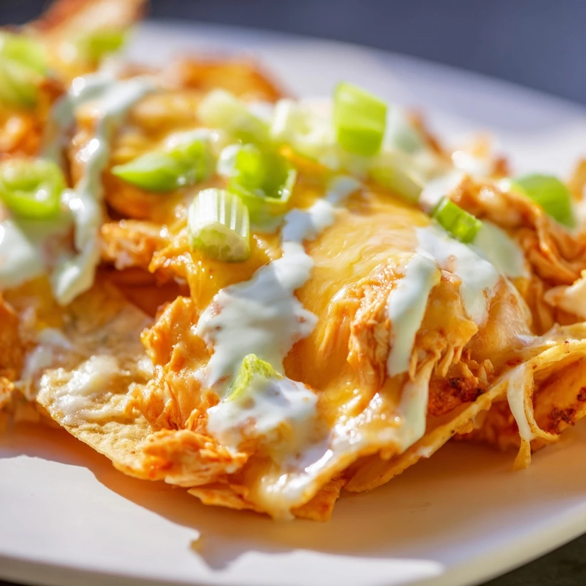 A close-up of Buffalo Chicken Nachos garnished with celery, tomatoes, and cilantro, served hot from the oven.