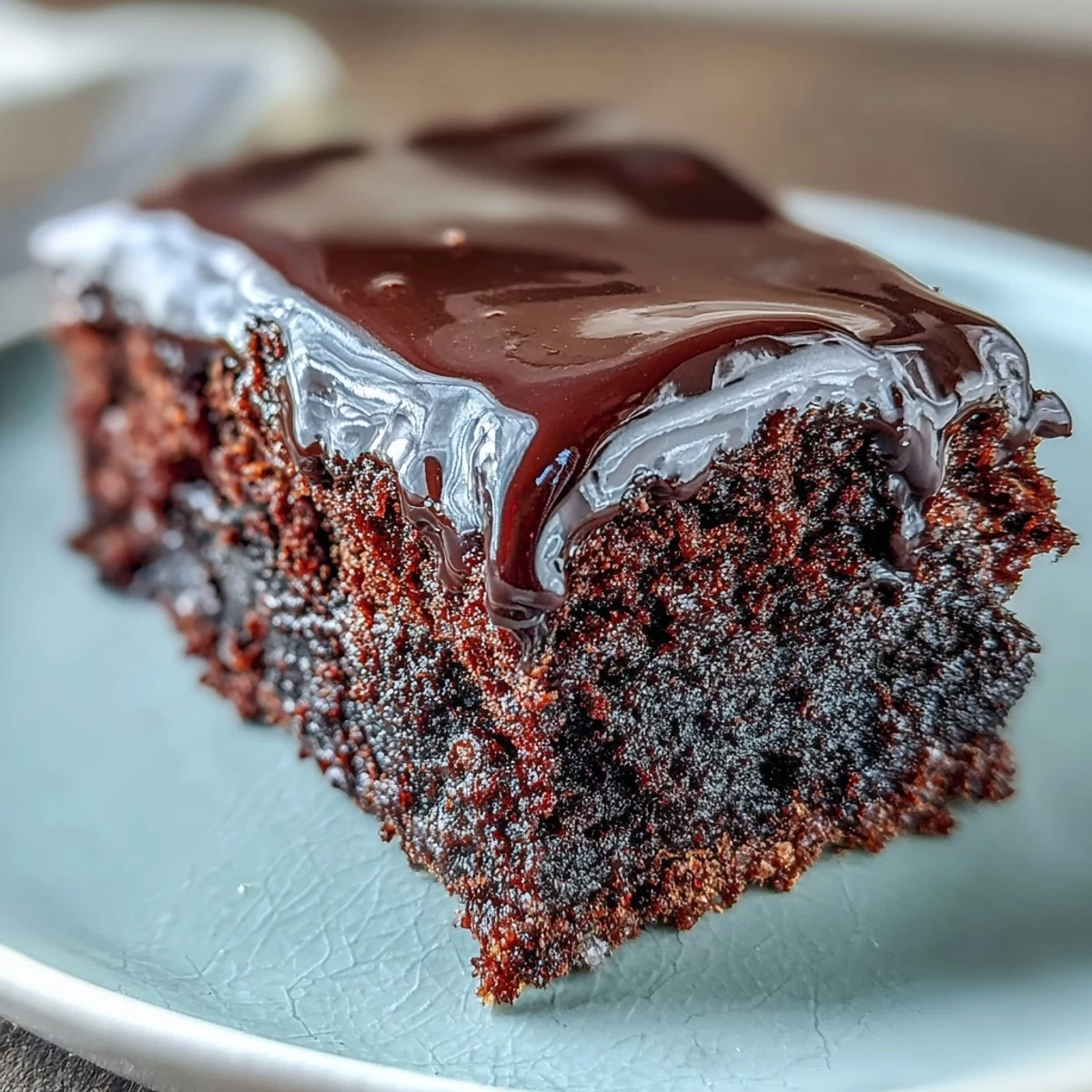 Close-up of Easy Chocolate Fudge Cake showing a squidgy texture, silky-smooth chocolate icing, and served on a white plate.