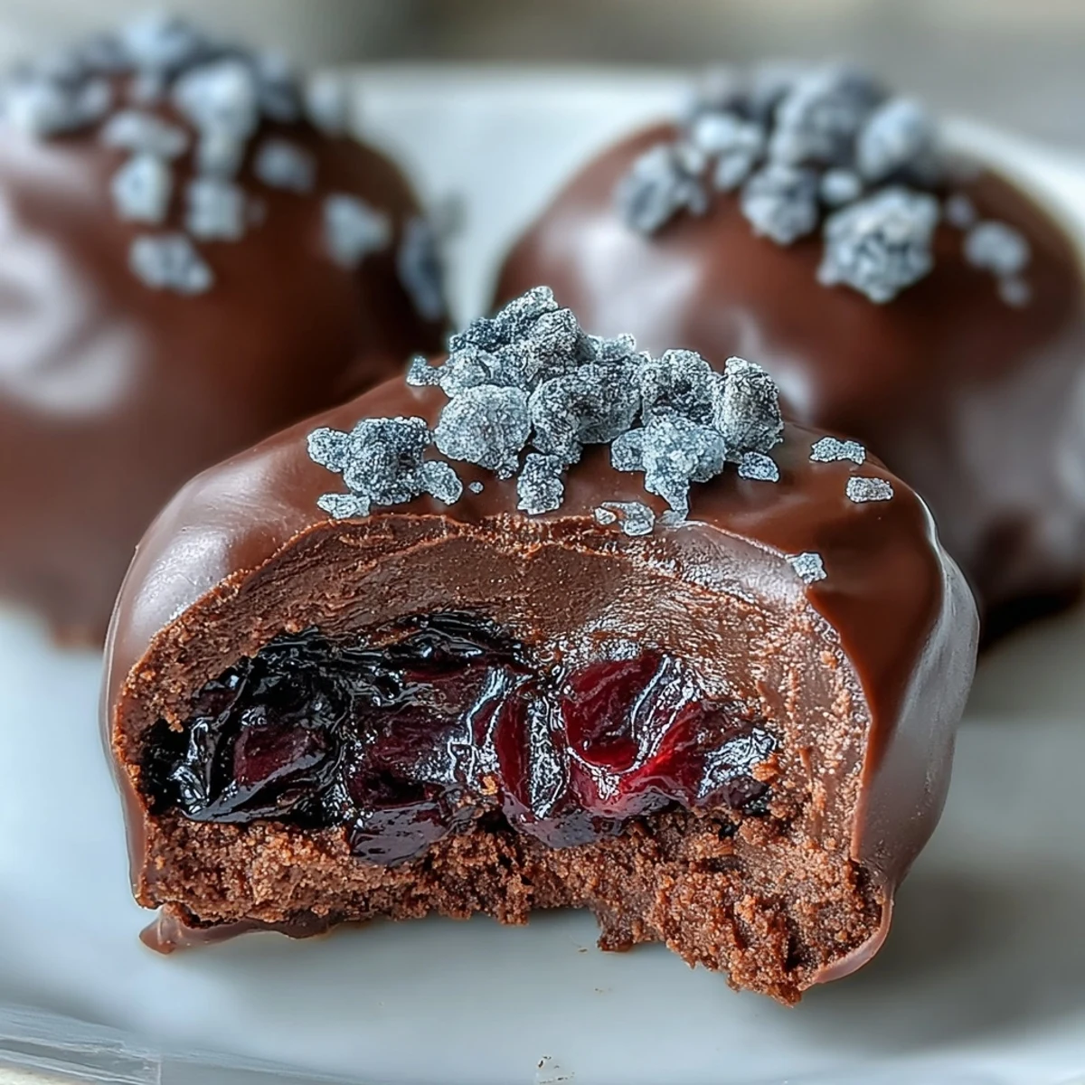 Luscious Black Currant Chocolate Truffles dusted with cocoa powder are arranged elegantly on a dessert plate near fresh berries.