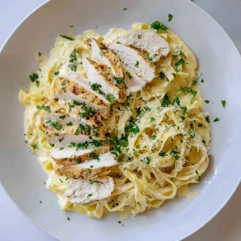Golden slices of Cajun Chicken Alfredo Fettuccine Pasta are tossed in a creamy, cheesy sauce, ready to serve.