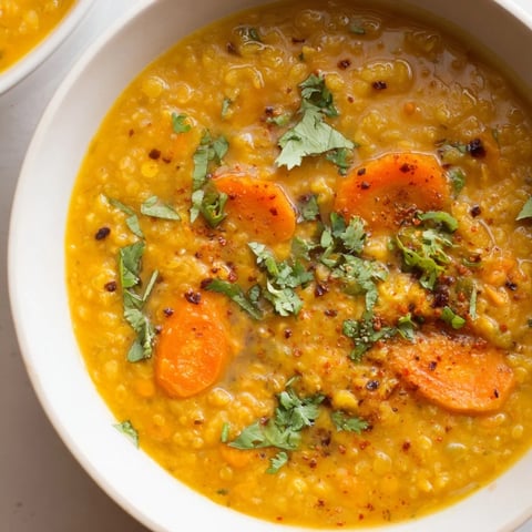Steaming bowl of Spiced Carrot Lentil Soup, vibrantly orange, with cilantro garnish and lemon wedges.