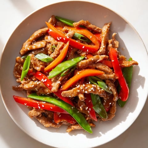 Sweet teriyaki pork stir-fry glistens with a savory sauce, alongside colorful bell peppers and carrots.