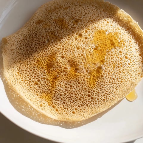 Golden, bubbly Moroccan Baghrir crepes are ready, drizzled with melted butter and sweet honey.