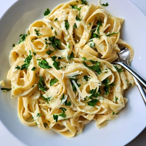 A bowl of Skinny Alfredo Garlic Parmesan Snowy Pasta with fresh parsley and extra Parmesan sprinkles on top.