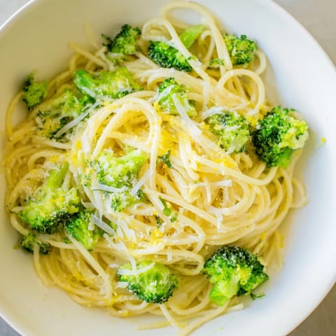 A close-up of one-pot lemon broccoli pasta shows al dente spaghetti coated in a creamy garlic sauce with fresh basil garnish.  