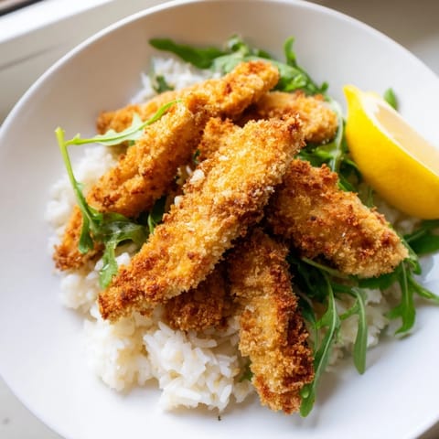A close view of a Crispy Parmesan Chicken Cutlet Bowl, with fresh lemon wedges and a drizzle of sauce.  