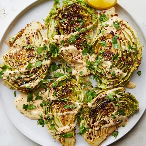 Roasted cabbage steaks drizzled with tahini, topped with sesame seeds and lemon wedges.  