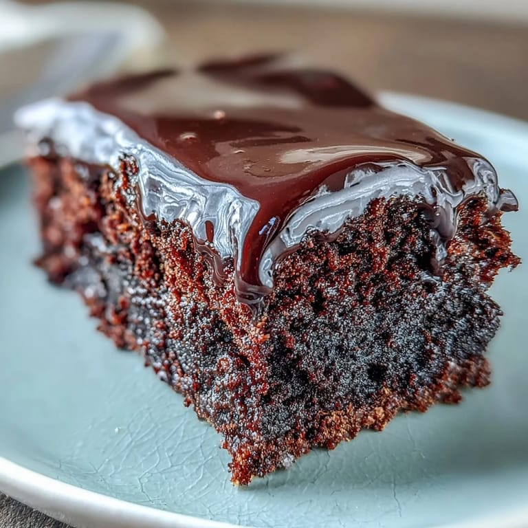 Close-up of Easy Chocolate Fudge Cake showing a squidgy texture, silky-smooth chocolate icing, and served on a white plate.