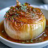 A bowl of tender, simmered onions in a fragrant, buttery spiced broth, garnished with fresh parsley and chives.